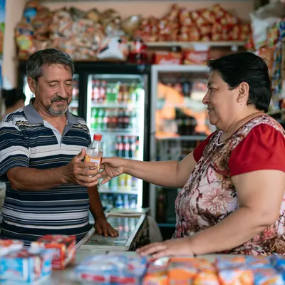 Beverages: a shopkeeper handing a bottled drink to a customer in a corner shop